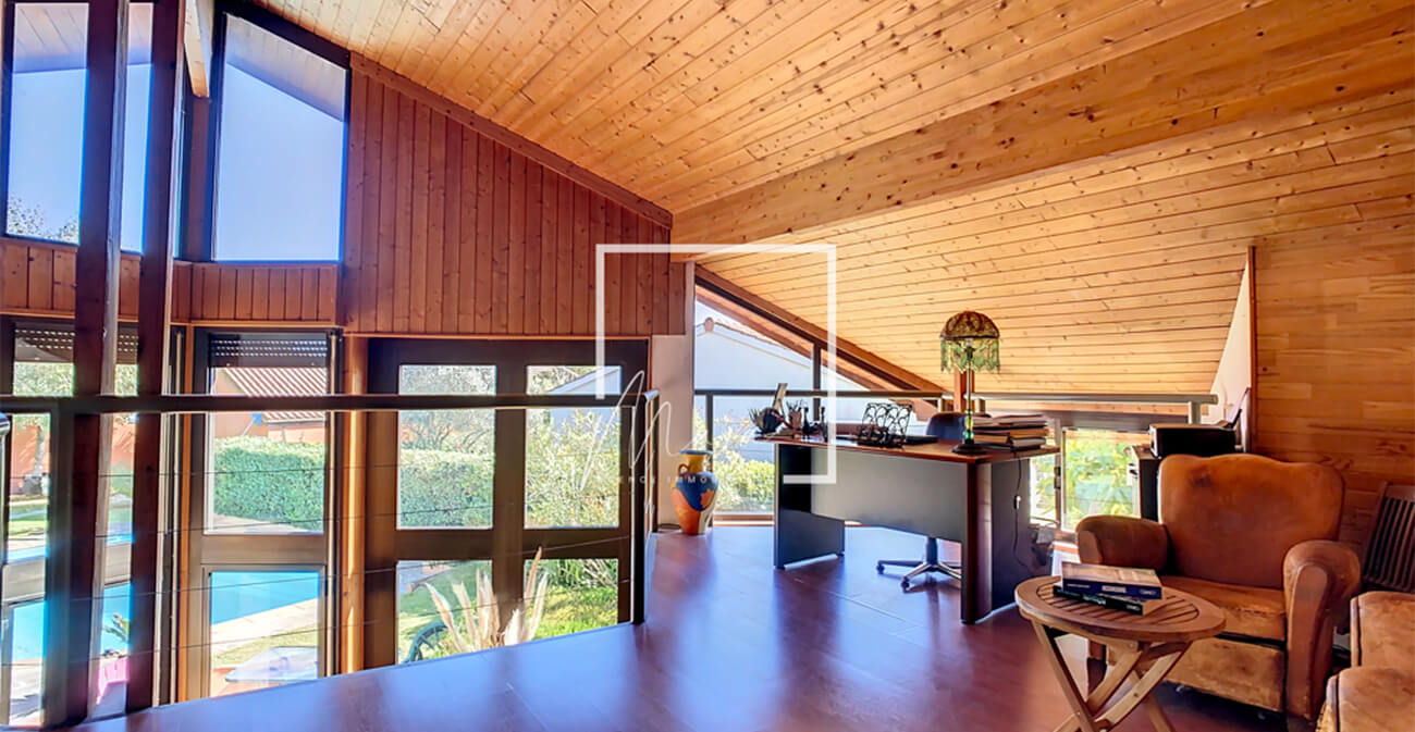 Etage ouvert d'une maison avec grandes fenêtres donnant sur une piscine, coin bureau et fauteuils marrons
