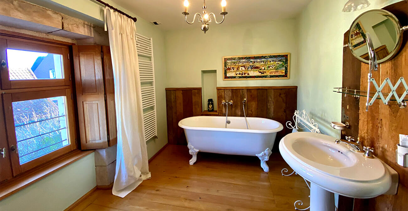 Salle de bain avec baignoire à pieds, lustre, tableau accroché au mur, miroir et lavabo avec une vasque unique